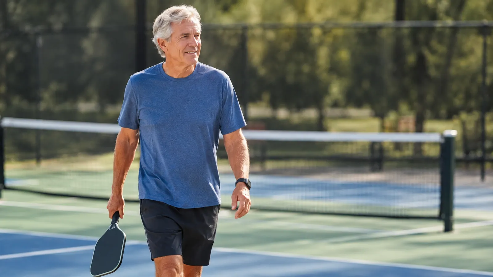 A man in his sixties walking off the court carrying a paddle, looking relaxed