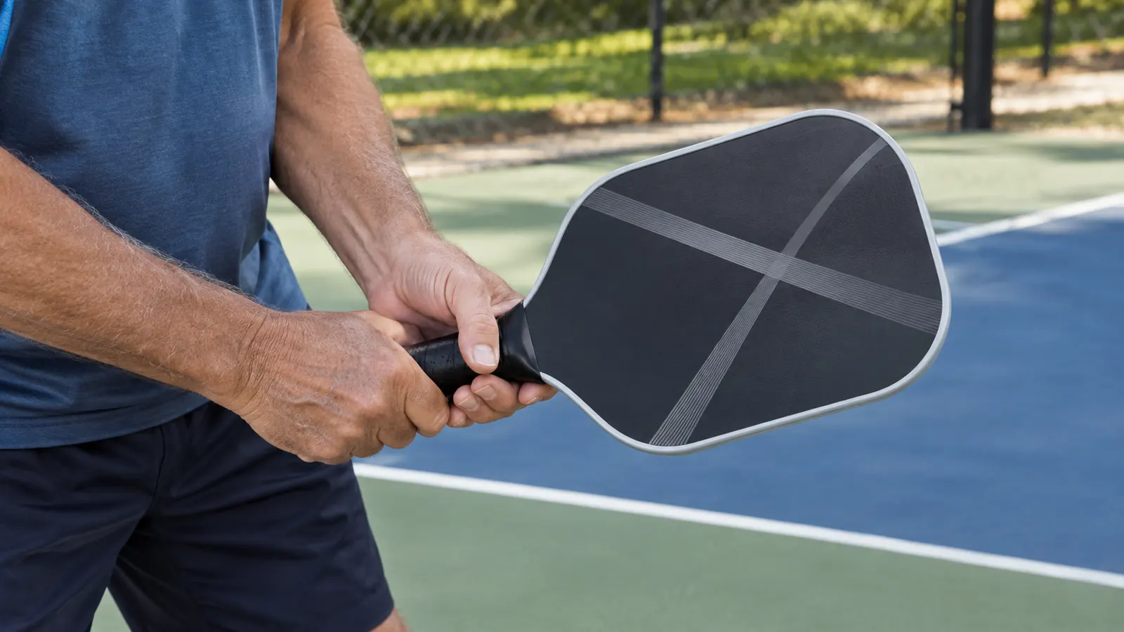 A player's hands adjusting the grip on a pickleball paddle at the kitchen line