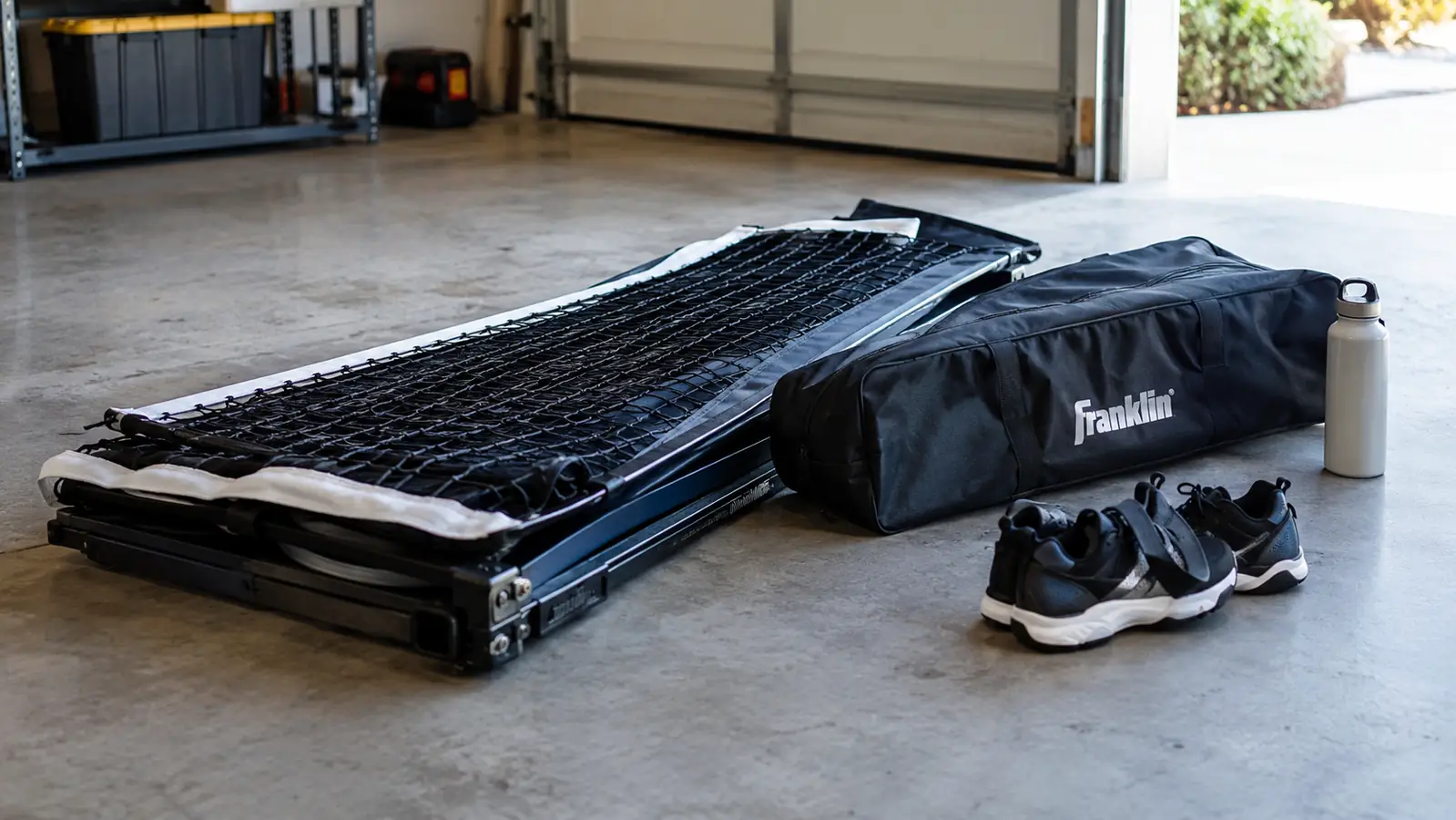 A portable pickleball net folded flat with its carrying bag beside it on a garage floor