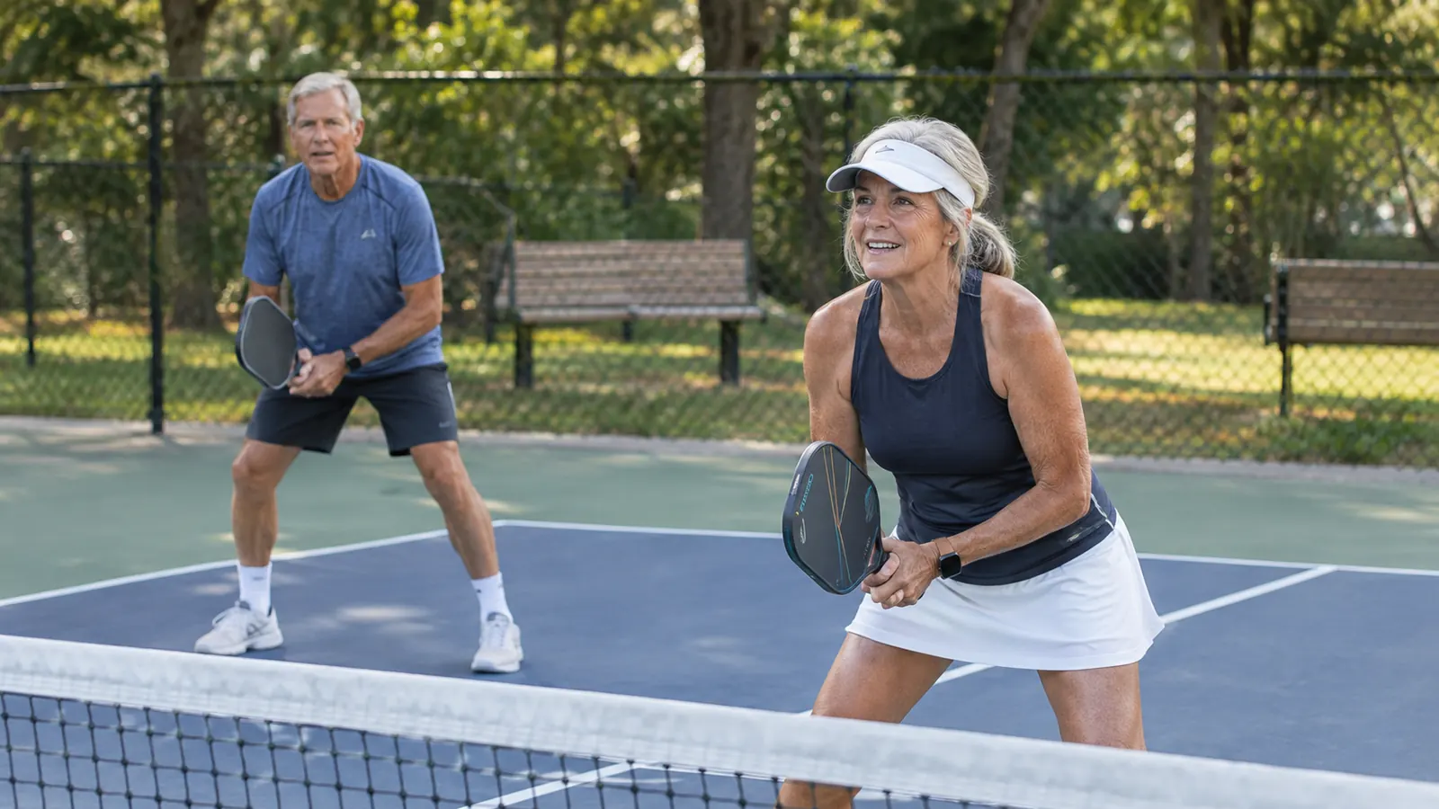 A couple in their sixties playing pickleball doubles on a park court.